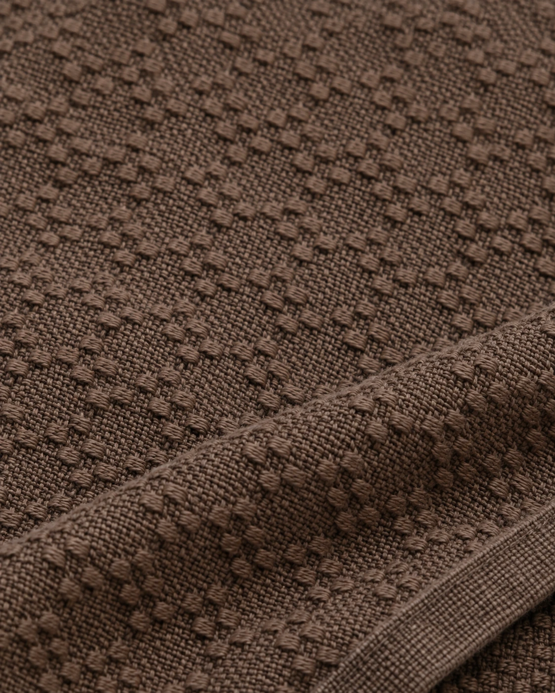 Cocoa huckaback fabric with short raised yarn floats and a compact repeating woven texture